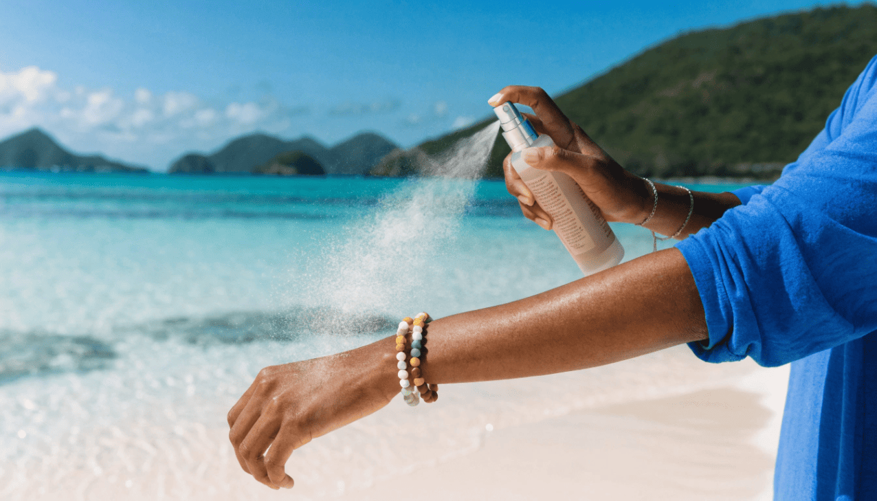 A person applying sunscreen with a fine mist spray evenly covering the skin in a smooth and controlled way